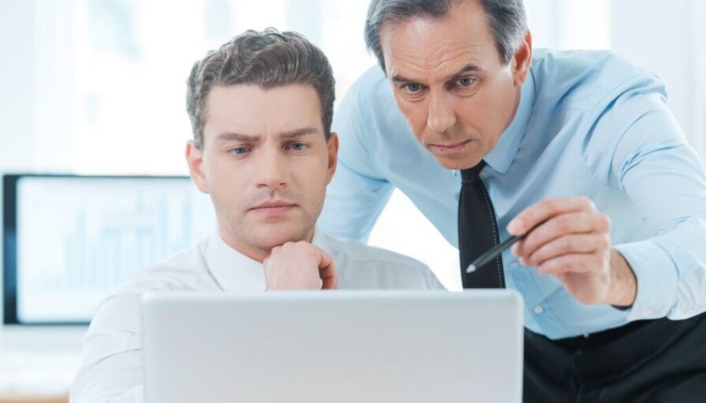 Two business men in suits looking at process efficiency on a laptop together,